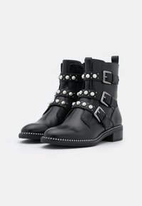 Botas de tobillo de cuero negro con hebillas y acentos de perlas. Cuentan con una puntera redondeada y un tacón bajo y cuadrado, decoradas con un ribete de tachuelas.