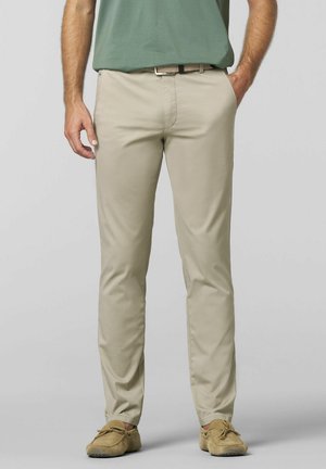 Beige chinos with a slim fit, featuring smooth fabric, side pockets, and a discreet front seam. Worn with a green shirt and tan slippers.