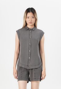 Grå ermeløs skjorte med knapper og krage, med buet kant, kombinert med matchende shorts. Laget av myk stoff med synlige sømdetaljer.