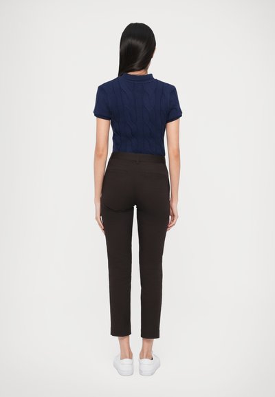 Μπλε σκούρο πλεκτό πόλο με κοντά μανίκια, με ανάγλυφο σχέδιο καλωδίου, συνδυασμένο με καφέ στενά παντελόνια και λευκά αθλητικά παπούτσια.