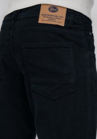 Corduroy broek in donker navy met verticale ribbels. Voorzien van een leren merkpatch op de tailleband en achterzakken met decoratieve stiksel.