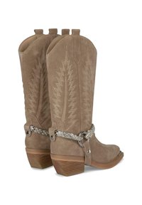 Stivaletti in camoscio marrone chiaro con cuciture decorative, punta appuntita e tacco in legno impilato. Presentano un cinturino intrecciato argentato con dettagli metallici.