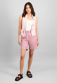 Rosa bomullsshorts med høy midje, frontlommer og rullede skjæringer. Kombinert med en hvit tanktopp og en lys rosa genser drapert over skuldrene.