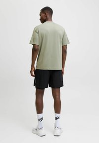 Camiseta de manga corta verde claro, pantalones cortos deportivos negros, zapatillas blancas y calcetines estampados; textura suave, corte relajado, diseño minimalista.