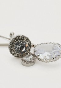 Boucles d'oreilles en métal argenté ornées de trois strass clairs de formes variées : un rond, une goutte et un ovale plus grand, tous montés dans des sertissages ornés.
