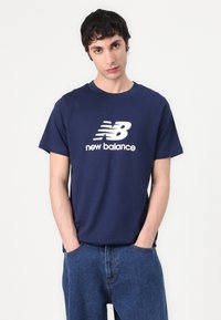 Sötétkék pamut póló kerek nyakkal, nagy, fehér "New Balance" logóval az elején. Kényelmes szabású.