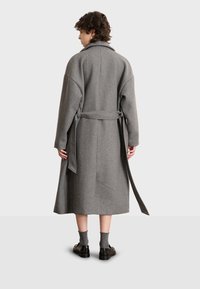 Abrigo de mezcla de lana gris con cintura ceñida por un cinturón, mangas largas y largo por debajo de la rodilla. Presenta un collar clásico y un acabado texturizado.
