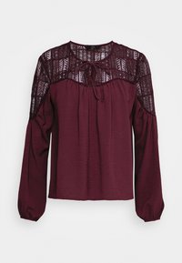 Bourgogne bluse med lange, pufrede ærmer, der har en tekstureret blonde yoke og bindebånd ved halsen. Blødt stof med en afslappet pasform.