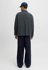 Giacca a scacchi in cotone bianco e nero con vestibilità ampia, abbinata a pantaloni navy a gamba larga. Presenta un colletto aperto e dettagli con bottoni.