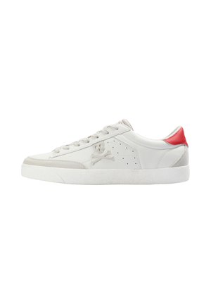 Zapatilla baja blanca con acentos de ante gris claro, una lengüeta trasera roja, logo de calavera y huesos cruzados en el lateral, y suela de goma blanca.