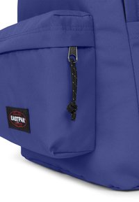 Blå ryggsäck med en texturerad tyg, med en framficka och en svart dragkedjehandtag. Visar Eastpak-logotypen på en svart lapp.