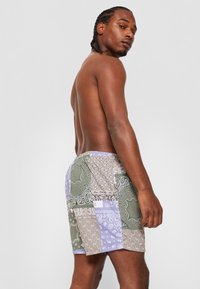 Pantaloni scurți de înot din material patchwork, în verde, mov și bej, cu modele de bandană; talie elastică, buzunare laterale și o croială lejeră.