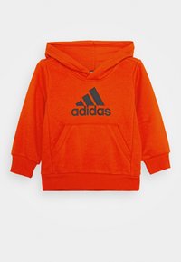 Oranje hoodie van zachte stof, met een kangoeroezak en een zwart Adidas-logo op de voorkant. Relaxte pasvorm, ribgebreide manchetten.