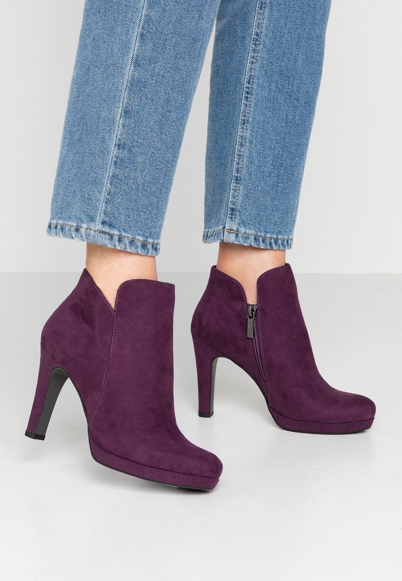 Bottines en daim violet avec bout pointu, talon haut et fermeture éclair latérale ; présentent une découpe au niveau de la cheville pour un look moderne.