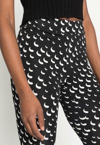 Leggings pretos com um padrão repetido de lua crescente branca, com uma textura suave e elástica e um cós alto para conforto.