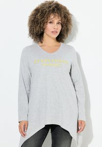 Helles graues Langarm-Tunikakleid mit V-Ausschnitt, das mit gelber Schrift "ALLES hat Schönheit" bedruckt ist. Asymmetrischer Saum, weicher Stoff.