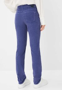 Lilla kordfløjlsbukser med lige ben, med to baglommer og en tekstureret stof. Båret med hvide sneakers.