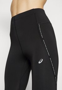 Leggings sportivi neri con una vita alta, caratterizzati da accenti laterali riflettenti. Realizzati in materiale elasticizzato per una silhouette aderente.