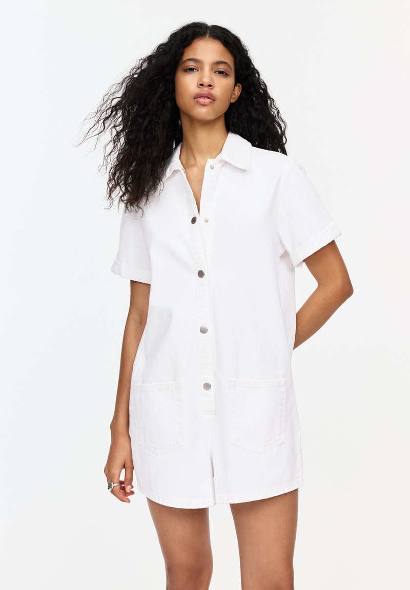 Witte denim jurk met kraag, korte mouwen, knoopsluiting aan de voorkant en twee voorzakken. Licht ontspannen pasvorm en minimale stikdetails.