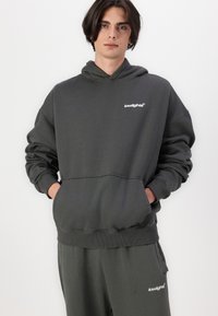 Charcoal gray hoodie with a front pocket, ribbed cuffs, and hem. Features a white logo on the left chest. Material appears soft and textured.