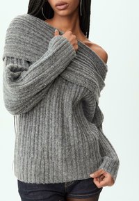 Grauer gerippter Pullover mit schulterfreiem Design und weiten Ärmeln. Hergestellt aus weichem Material mit strukturierter Oberfläche.