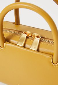 Yellow leather handbag featuring two short handles, a zipper closure with gold hardware, and embossed logo detailing on the zipper pulls.