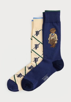 Two pairs of crew socks, one cream with green and navy patterns, one navy with a vintage-style bear in a beige outfit and hat.