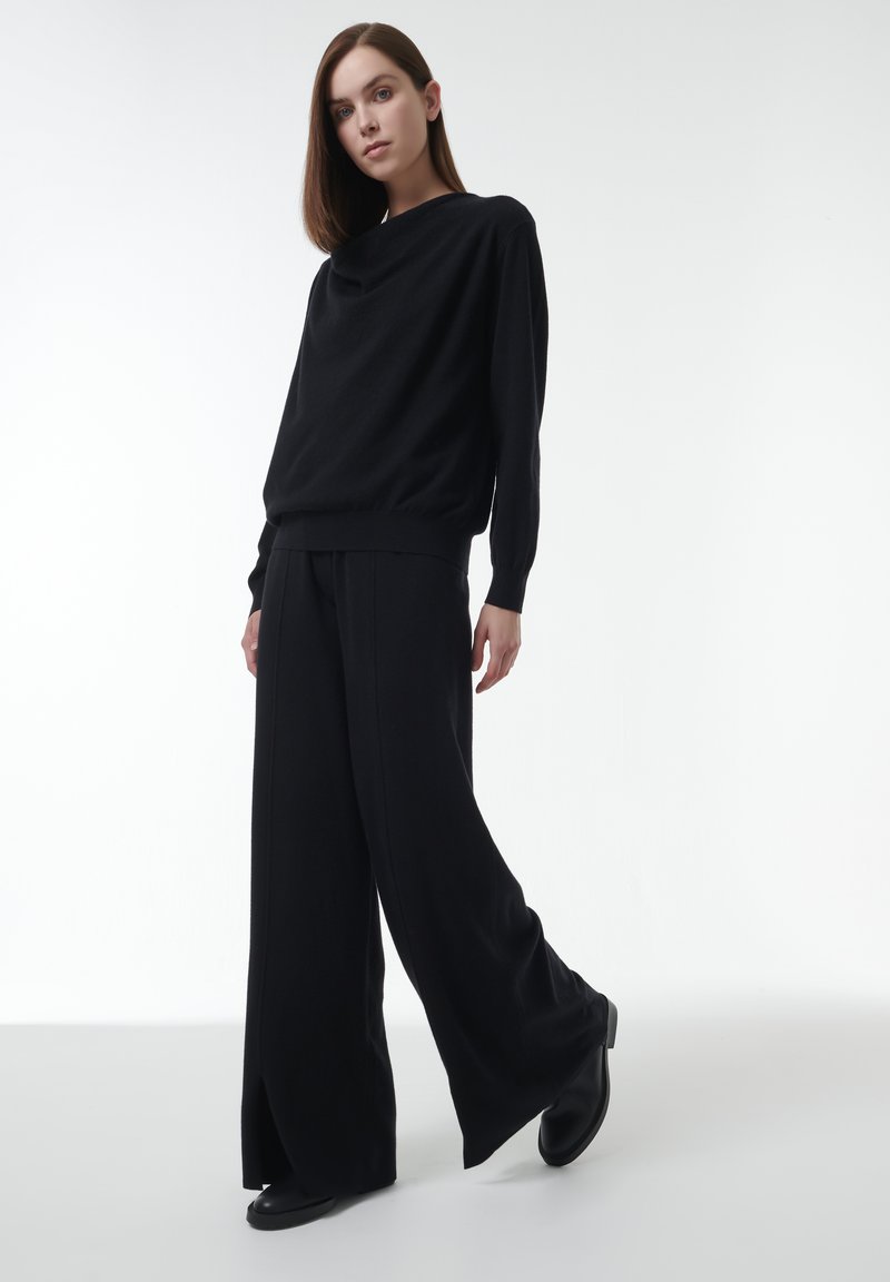 Zwarte gebreide trui met een relaxed fit en brede mouwen, gecombineerd met zwarte wijde broek met zijsplitten. Soepele, zachte textuur.