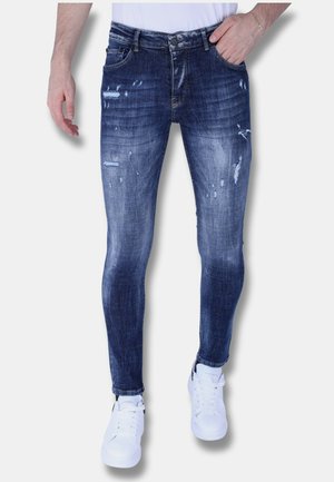 Smal fit, donkerblauwe denim jeans met versleten details en wassing. Bevat vijf zakken en een knopenstrip sluiting. Gepaard met witte sneakers.