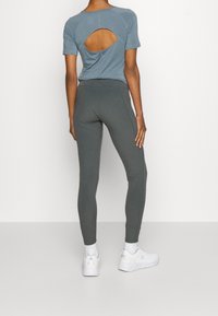 Haut bleu clair à manches courtes avec une découpe au dos, associé à un legging gris foncé, tous deux fabriqués dans un tissu extensible, complété par des chaussures de sport blanches.
