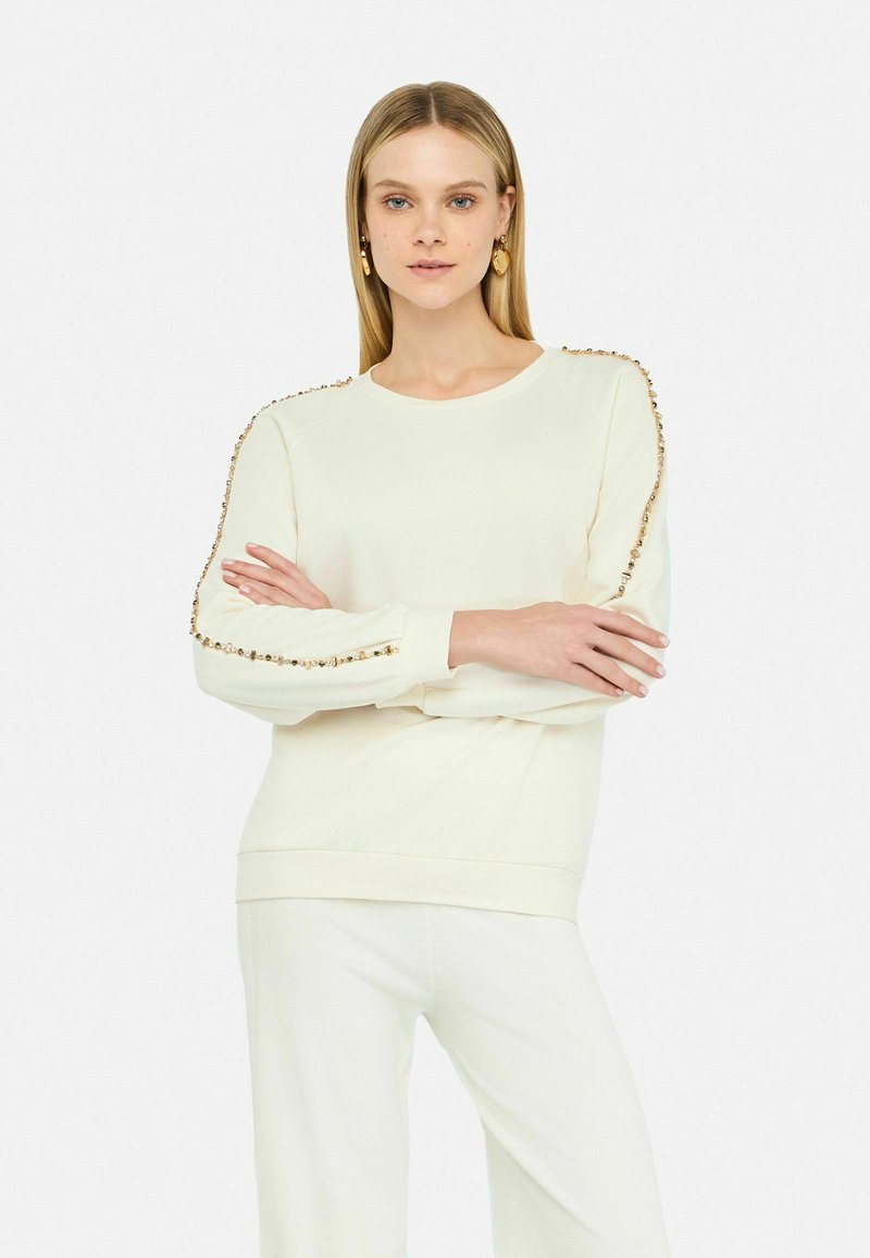 Felpa color crema con collo rotondo, caratterizzata da dettagli decorativi lungo le maniche e polsini e orlo a costine.