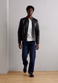 Black leather jacket, white t-shirt, blue denim jeans. Casual footwear with three stripes. Standing against a neutral background.
