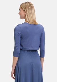 Niebieski krótki top z rękawami trzyczwartowymi, wykonany z miękkiego materiału. Posiada okrągły dekolt i jest połączony z długą, zwiewną suknią.