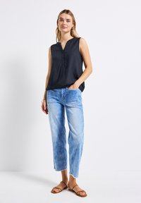 Top senza maniche nero con scollatura a V e pieghe sottili, abbinato a jeans blu chiaro dal taglio rilassato. I jeans presentano orli strappati e tasche.