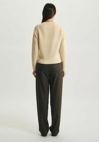 Un pull couleur crème avec un ourlet et des poignets côtelés, associé à un pantalon rayé foncé. L'accent est mis sur la vue arrière de la tenue.