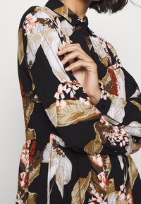Kwiatowa sukienka z długimi rękawami, czarna baza oraz kolorowe wzory liści i kwiatów w odcieniach brązu, pomarańczu i bieli. Zawiera kołnierzyk.