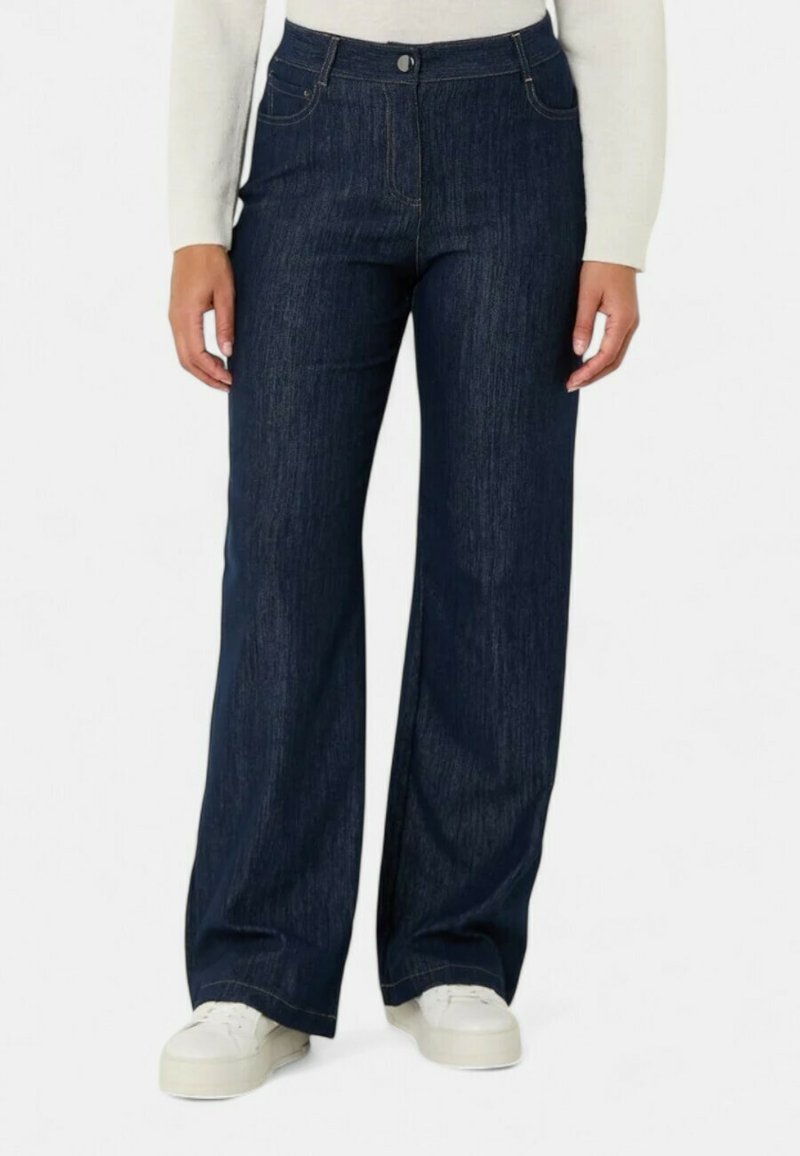 Jeans ampi in denim di colore blu scuro, con vita alta, tasche frontali e chiusura con bottoni classica, abbinati a sneakers bianche.