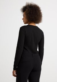 Sort langærmet top med rund halsudskæring, tætsiddende design og glat tekstur. Kombination med skræddersyede sorte bukser med baglommer.