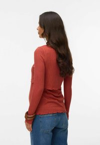 Ribbad långärmad topp i rostfärg, med en kortad design och vågig nederdel, stylead med högmidjade blåjeans.