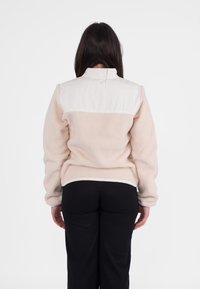 Fleecevest in lichtbeige met een wit doorgestikt schouderstuk en een hoge kraag. Heeft verlaagde schouders en elastische boorden. Accenten van gladde stof.