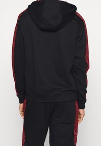 Sudadera negra con un estampado de leopardo rojo texturizado en los paneles laterales. Hecha de material suave, cuenta con capucha y puños acanalados.