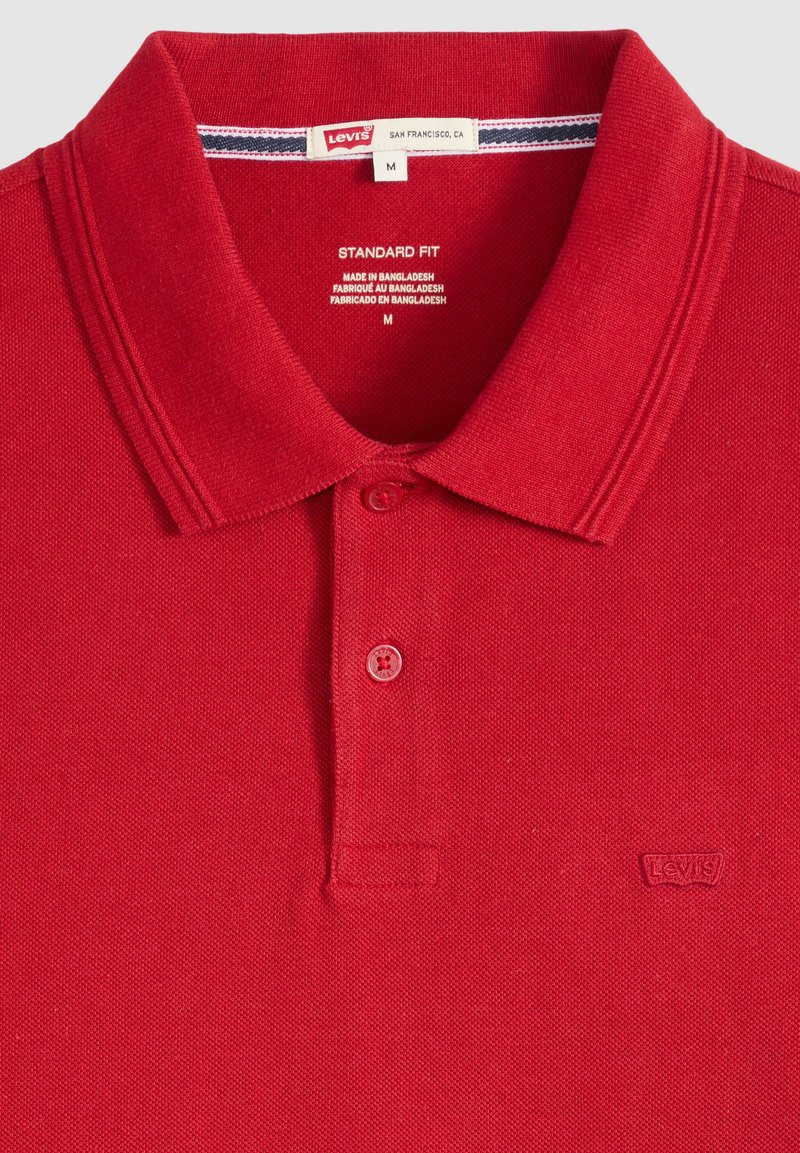 Polo rouge Levi's avec deux boutons, coupe standard, taille moyenne, fabriqué au Bangladesh, avec le logo Levi's brodé sur la poitrine.