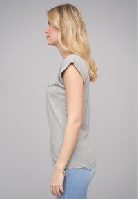 T-shirt gris à manches courtes en coton doux avec une silhouette ajustée, accompagné de jeans skinny bleu clair. Bracelet visible au poignet.