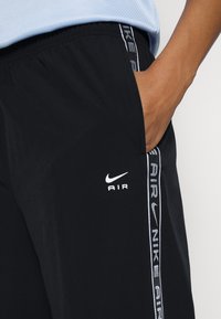 Sorte Nike shorts har et hvidt Nike-logo og "AIR" tekst på forsiden, med en hvid sidestreg der viser mærkenavnet. Blødt stof.