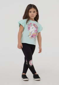 T-shirt azzurro chiaro con maniche arricciate e stampa di unicorno, abbinato a leggings neri con un design di unicorno sulla gamba inferiore. Sneakers nere.