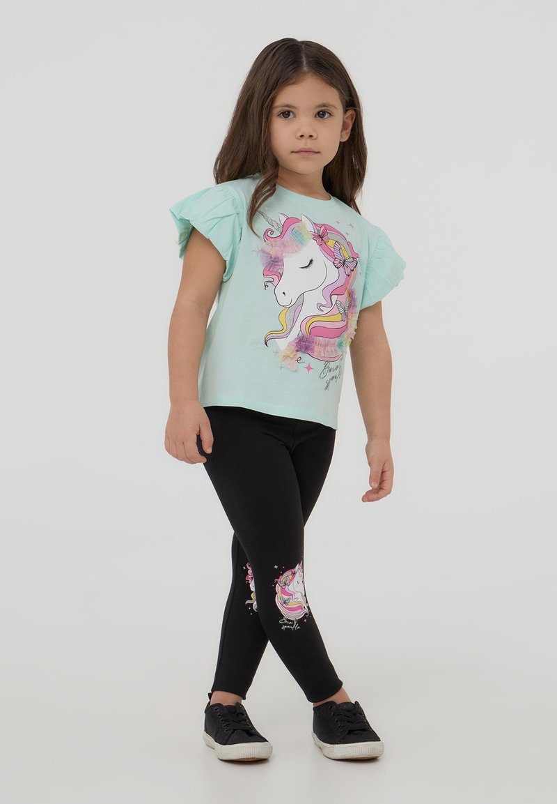 T-shirt azzurro chiaro con maniche arricciate e stampa di unicorno, abbinato a leggings neri con un design di unicorno sulla gamba inferiore. Sneakers nere.