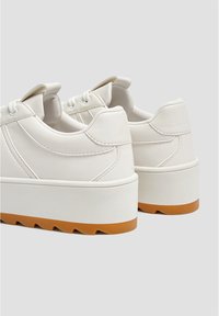 Baskets compensées blanches avec une finition lisse semblable au cuir, forme arrondie, semelle en gomme contrastante et détails renforcés au talon.