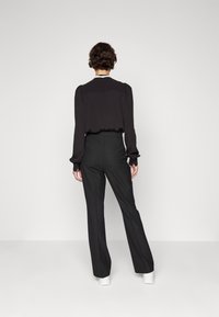 Svart långärmad blus med draperade axlar, tillsammans med högmidjade svarta byxor. Vita sneakers fulländar outfiten.