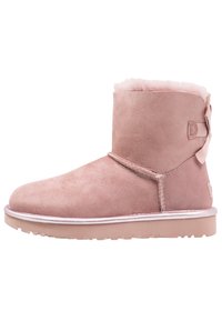 Różowe zamszowe botki za kostkę z miękkim futerkiem wewnątrz, płaską gumową podeszwą i ozdobną kokardką z tyłu; posiadają przeszywane akcenty i gładkie wykończenie.