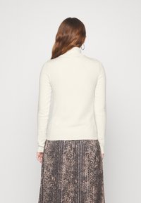 Cream-colored turtleneck sweater with long sleeves, fitted design, soft texture, worn over a patterned, ankle-length skirt.